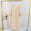 Beige Maxi-Abaya mit Blumenstickerei auf goldener Kleiderstange in einem hellen Raum.