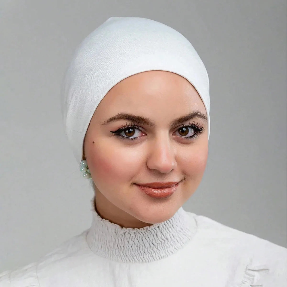 Una mujer vistiendo un gorro interior de hijab y una blusa deportiva blanca a juego.