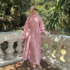 A woman wearing a pink elegant two-piece Arabic modest set stands next to a white railing outdoors.