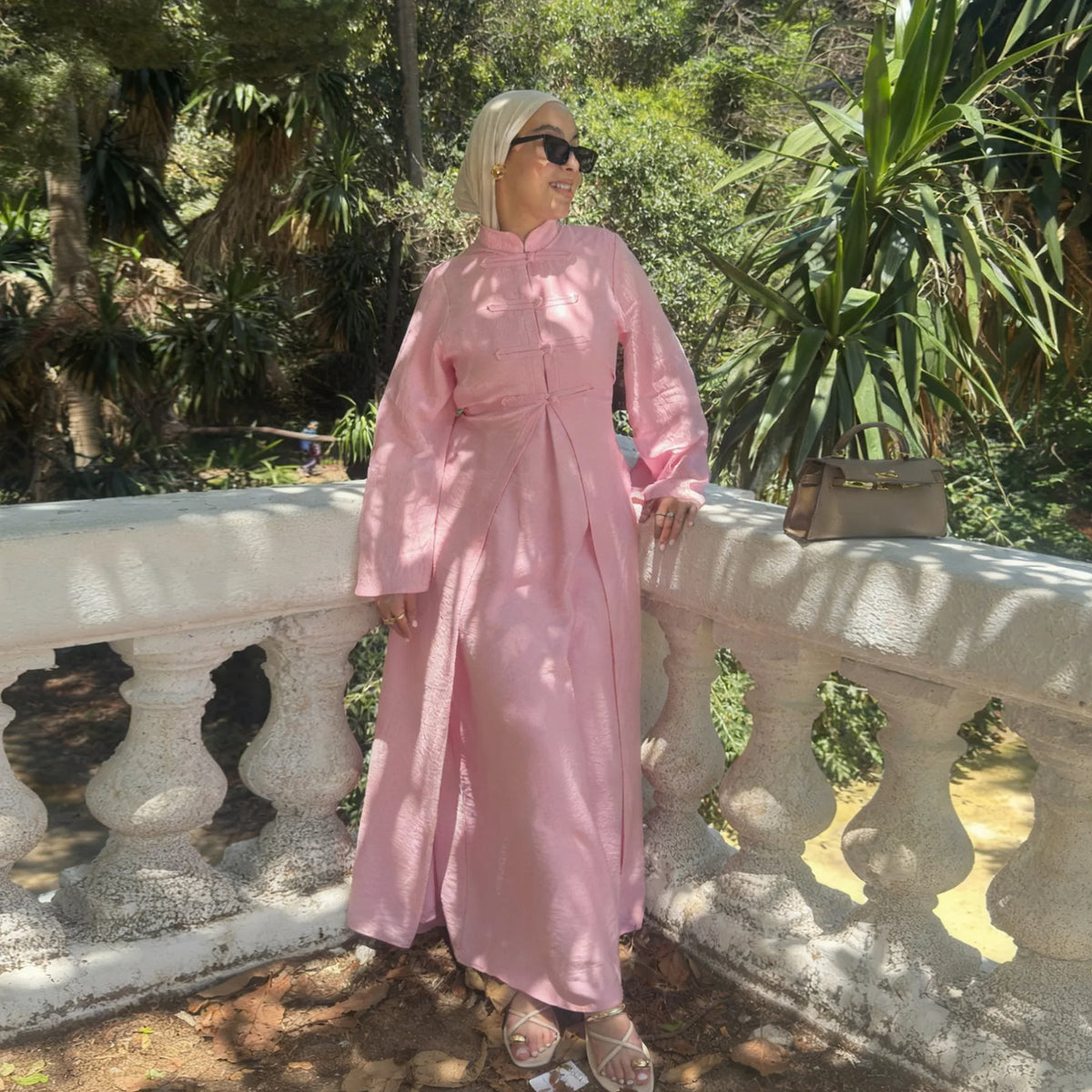 A woman wearing a pink elegant two-piece Arabic modest set stands next to a white railing outdoors.
