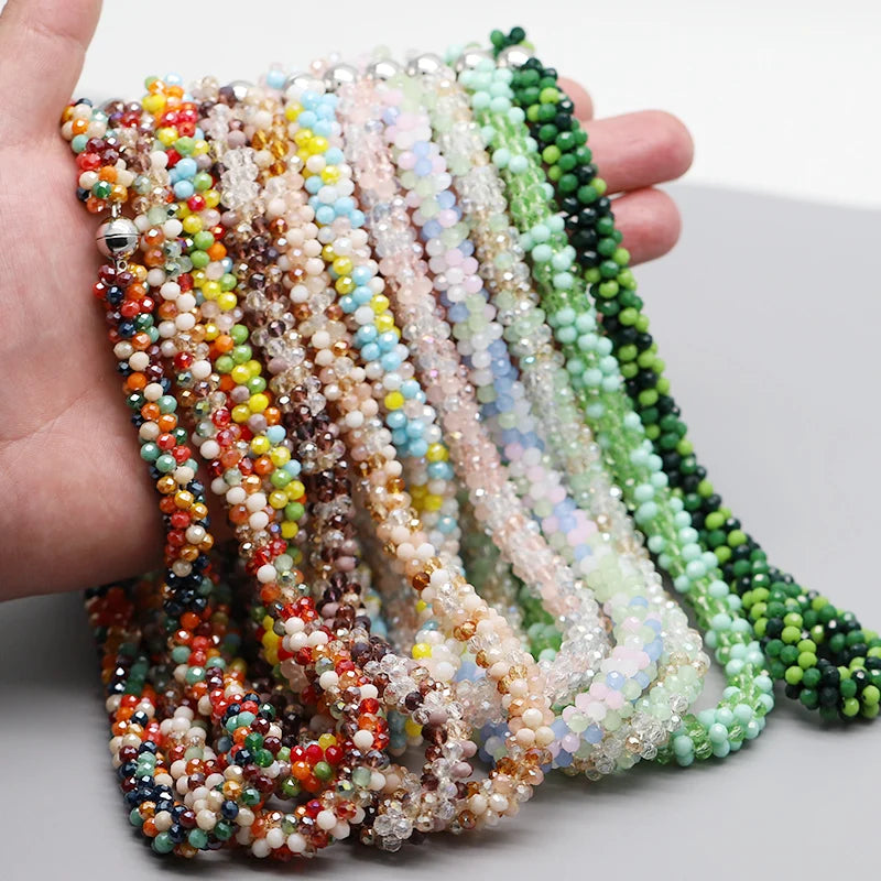 Eine Hand hält eine Sammlung farbenfroher, bohemienartiger geflochtener Perlenketten in verschiedenen Rosa-, Grün- und Braunt
