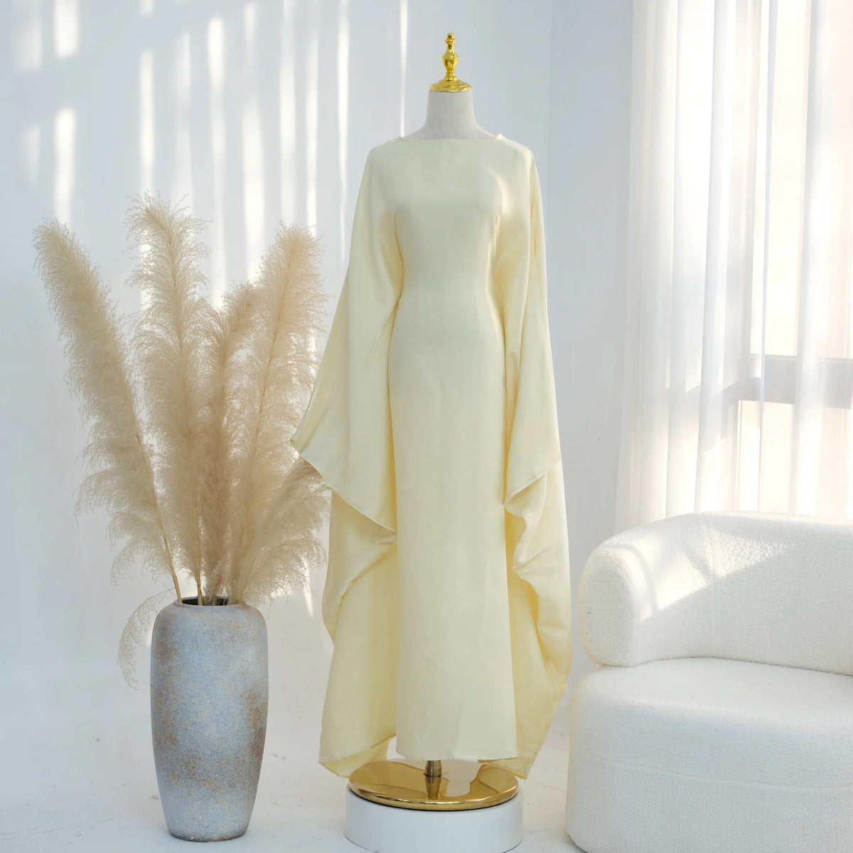 Elegant gelb-weißer Kaftan-Kleid auf einem Mannequin mit federartigen Schwänzen im Hintergrund.
