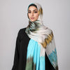 Eine Frau trägt einen bohemienartigen Aquarell-Hijabschal in Beige-, Grün- und Türkistönen über einem schwarzen Oberteil.