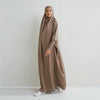 Eine Frau trägt eine lange, fließende taupe Abaya mit gerafften Ärmeln und Hijab.