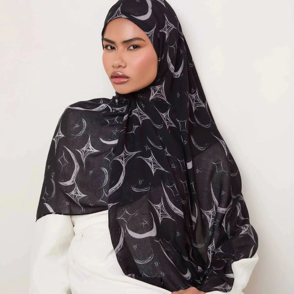 A woman wearing a black floral printed cotton hijab scarf with silver accents.