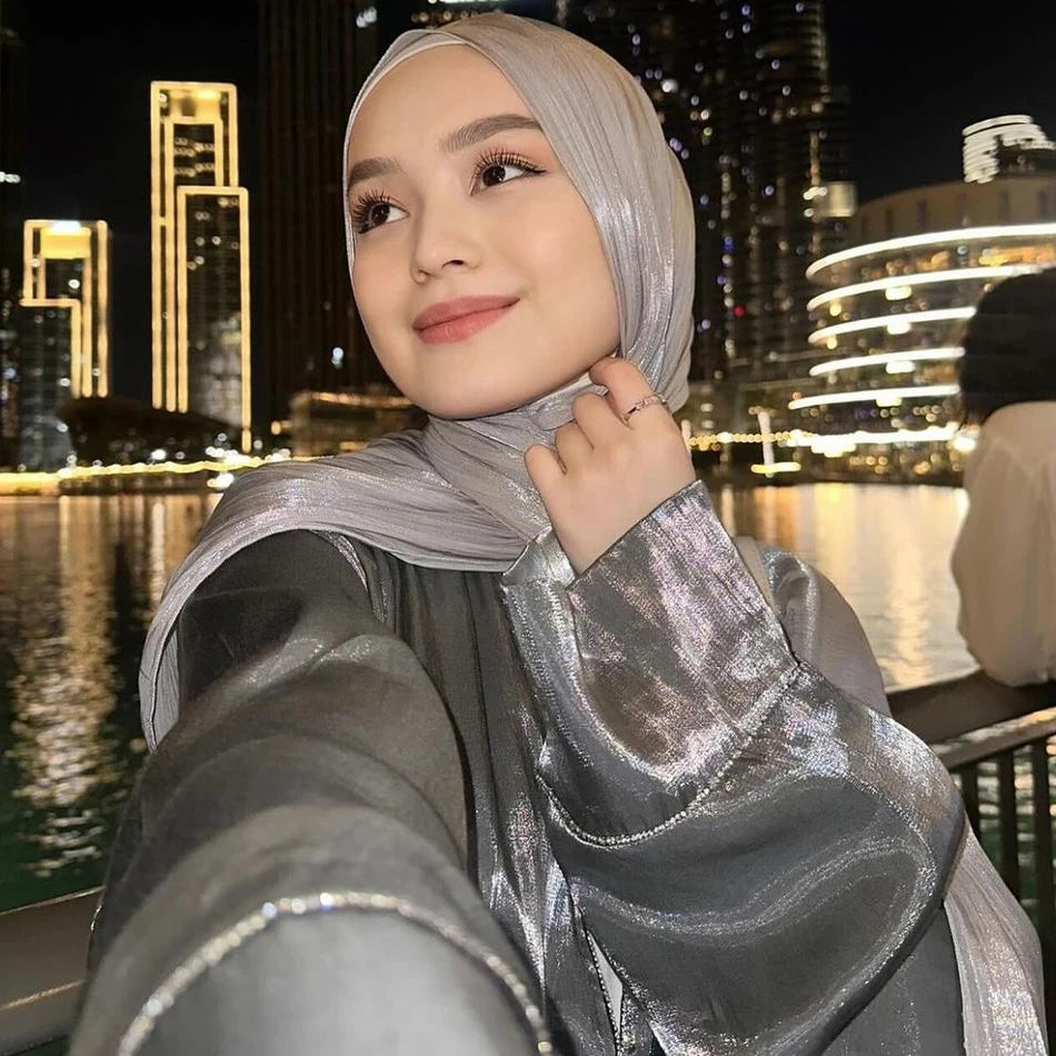Une femme portant un hijab en mousseline crinkle argentée et scintillante, regardant sur le côté dans un cadre extérieur de n
