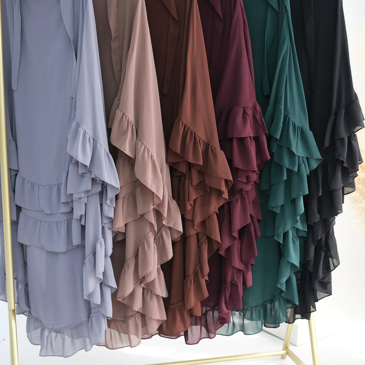 A display of ruffled two-layer chiffon hijabs in various muted tones including gray, brown, burgundy, and green.