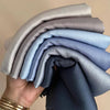 Eine Hand hält einen Stapel gefalteter Premium-Seiden-Hijabs in verschiedenen Blautönen und Grautönen.