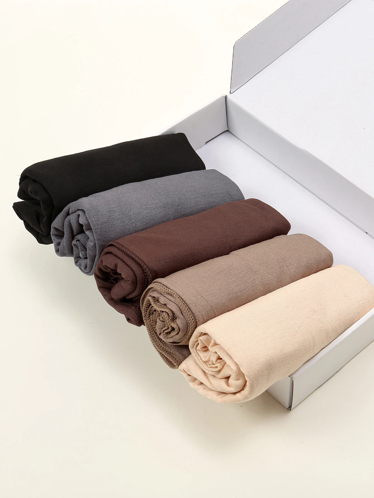 Ein Set aus fünf einfarbigen Jersey-Hijab-Schals in Schwarz, Grau, Braun, Beige und Tan präsentiert in einer weißen Box.