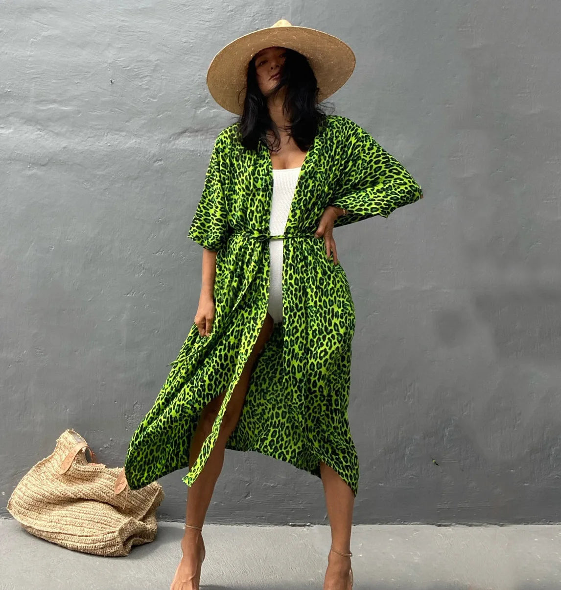 Eine Frau in einem leuchtend grünen Leopardenmuster-Sommer-Strandkimono und einem Strohhut vor einer grauen Wand.