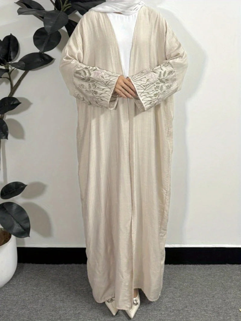 Beige lockere Kaftan-Abaya mit bestickten Ärmeln und weißem Hijab auf einem Hänger.