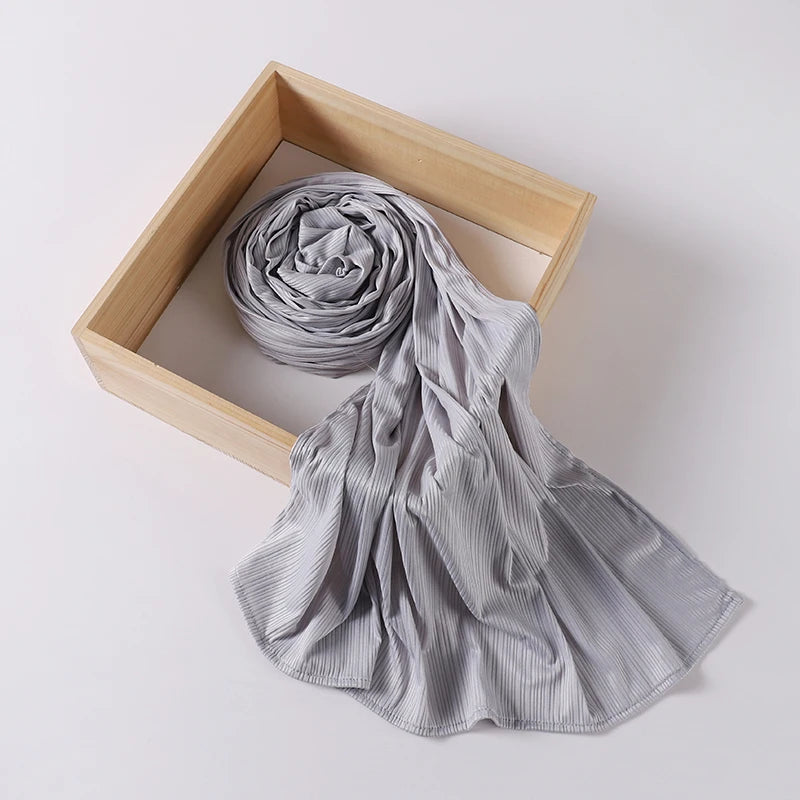 A gray ribbed jersey hijab scarf is rolled and draped within a light wooden frame.