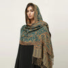 Una mujer modela un pañuelo pashmina de lujo con estampado verde azulado y dorado sobre su cabeza y hombros.