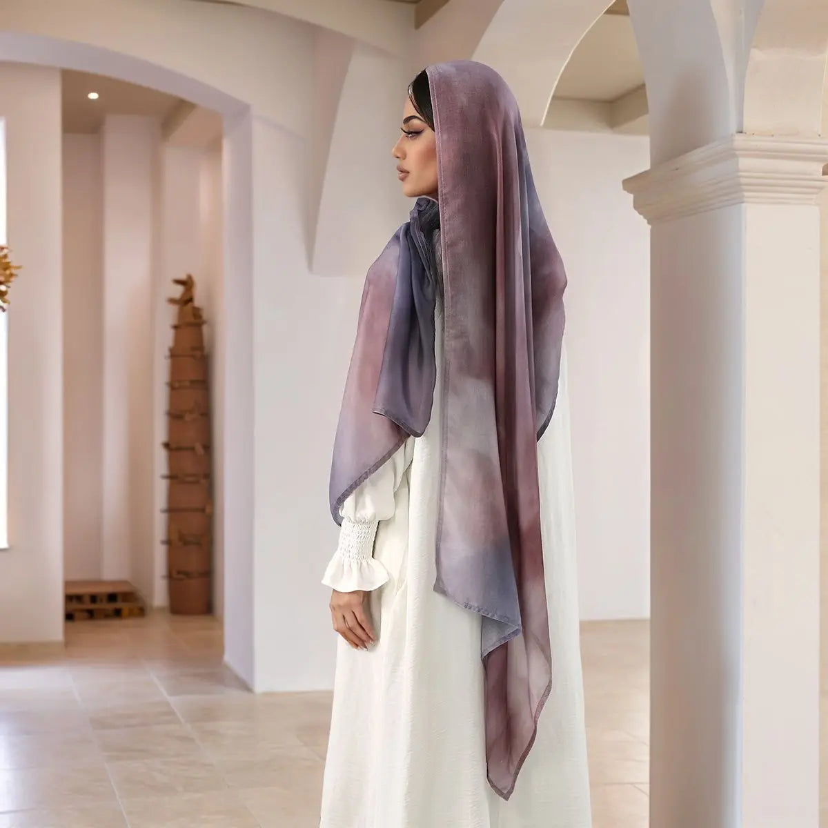 A woman wearing a white dress and a purple watercolor print modal scarf stands in a bright, modern interior.