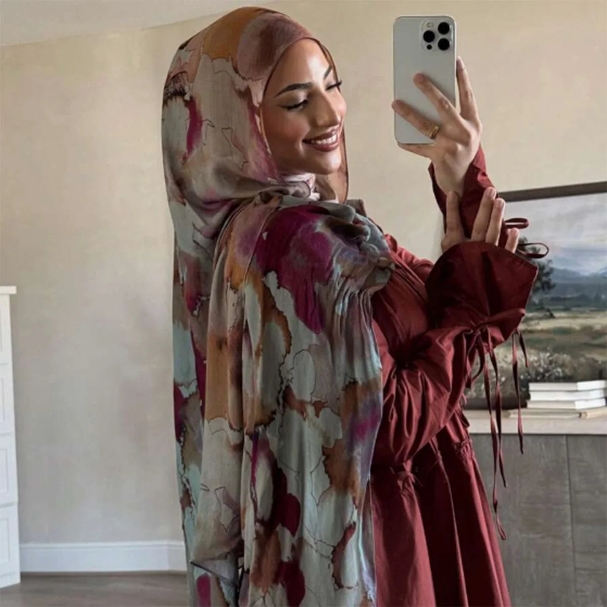 Eine Frau trägt einen Aquarelldruck-Baumwoll-Leinen-Hijab und ein dunkelrotes Kleid und macht ein Selfie.