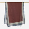 A maroon linen hijab scarf with a light blue patterned border hanging on a rod.