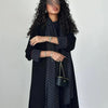 Eine Frau trägt ein elegantes schwarzes Polka-Dot-Abaya-Cardigan-Kleid mit langen Ärmeln und einem dunklen Oberteil.