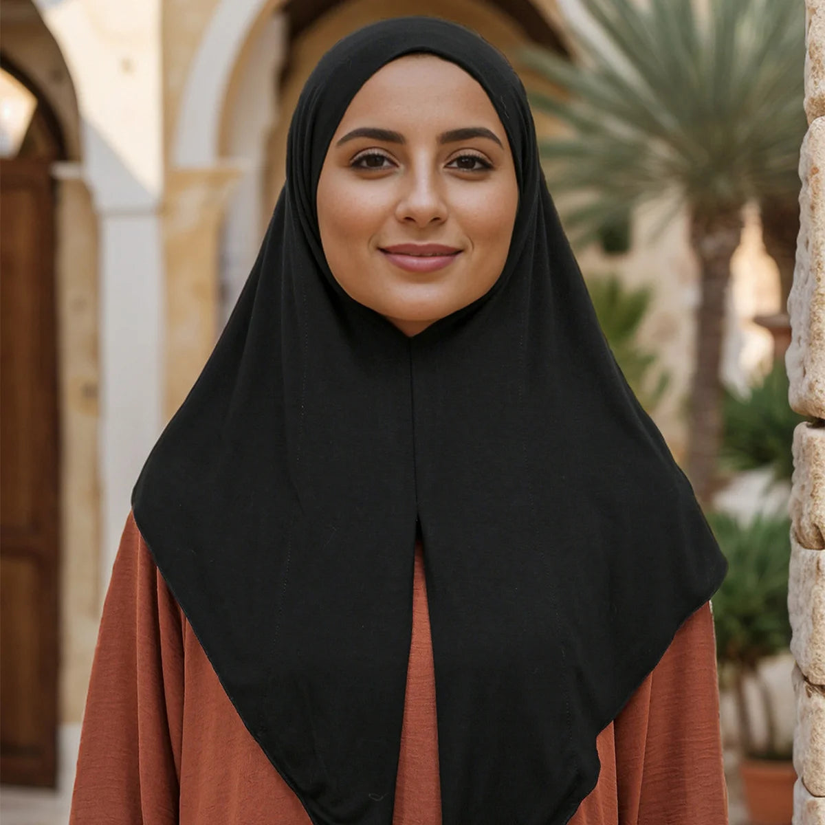 Une femme portant un foulard instant noir sur un haut orange, souriant à la caméra.