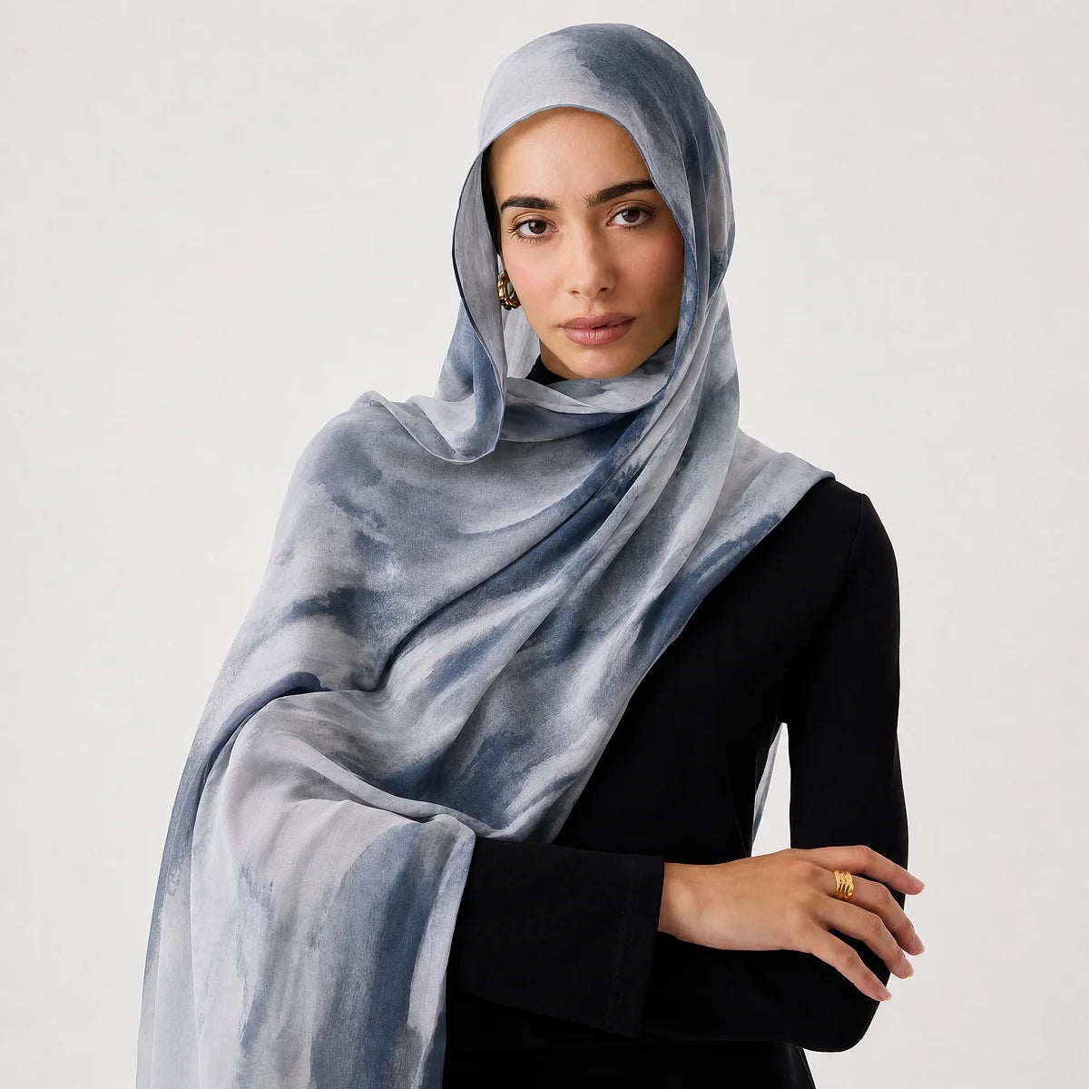 Eine Frau trägt einen hellblauen und grauen Aquarell-Schal als Hijab über einem schwarzen Oberteil.