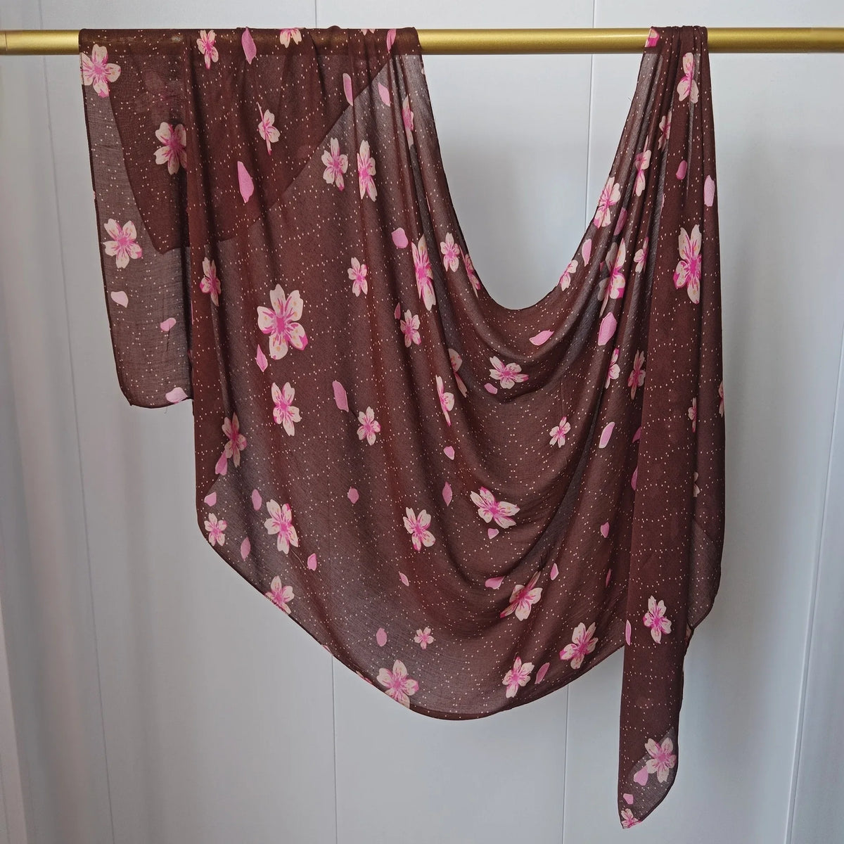 Dunkelbraner, durchscheinender Hijab-Schal mit rosa Blumenmuster an einem goldenen Stab hängend.