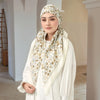 Eine Frau trägt einen cremefarbenen und goldenen Blumenmuster-Voile-Hijab und ein weißes Oberteil.