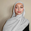 Eine Frau trägt einen hellgrauen Gradienten-Rayon-Modal-Hijab-Schal um den Hals und Kopf.