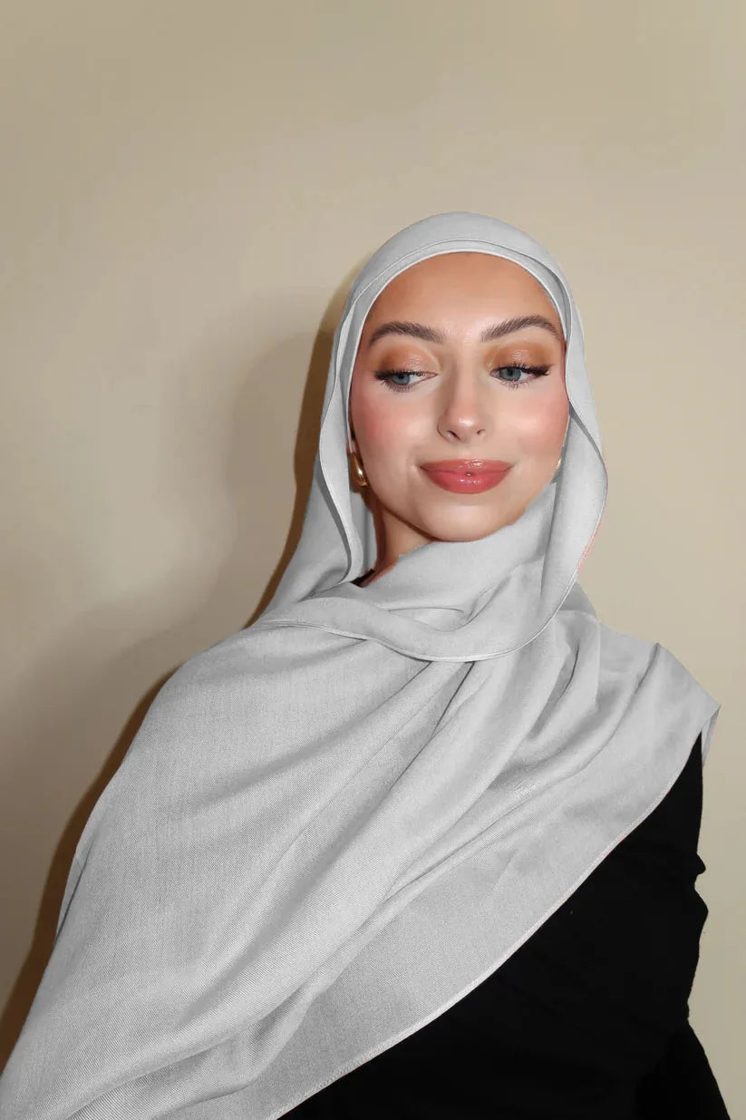 Eine Frau trägt einen hellgrauen Gradienten-Rayon-Modal-Hijab-Schal um den Hals und Kopf.