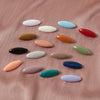 Una selección de ocho chinchetas y pinzas para pañuelos de forma ovalada en varios colores pastel y vibrantes sobre un fondo 