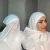 A woman wearing a white chiffon instant hijab with a modal cotton cap, looking towards the camera.