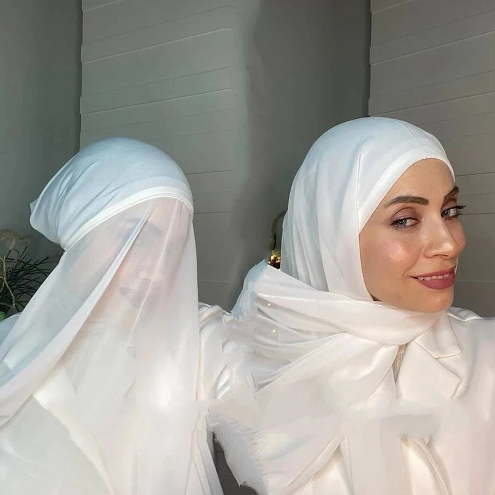 A woman wearing a white chiffon instant hijab with a modal cotton cap, looking towards the camera.