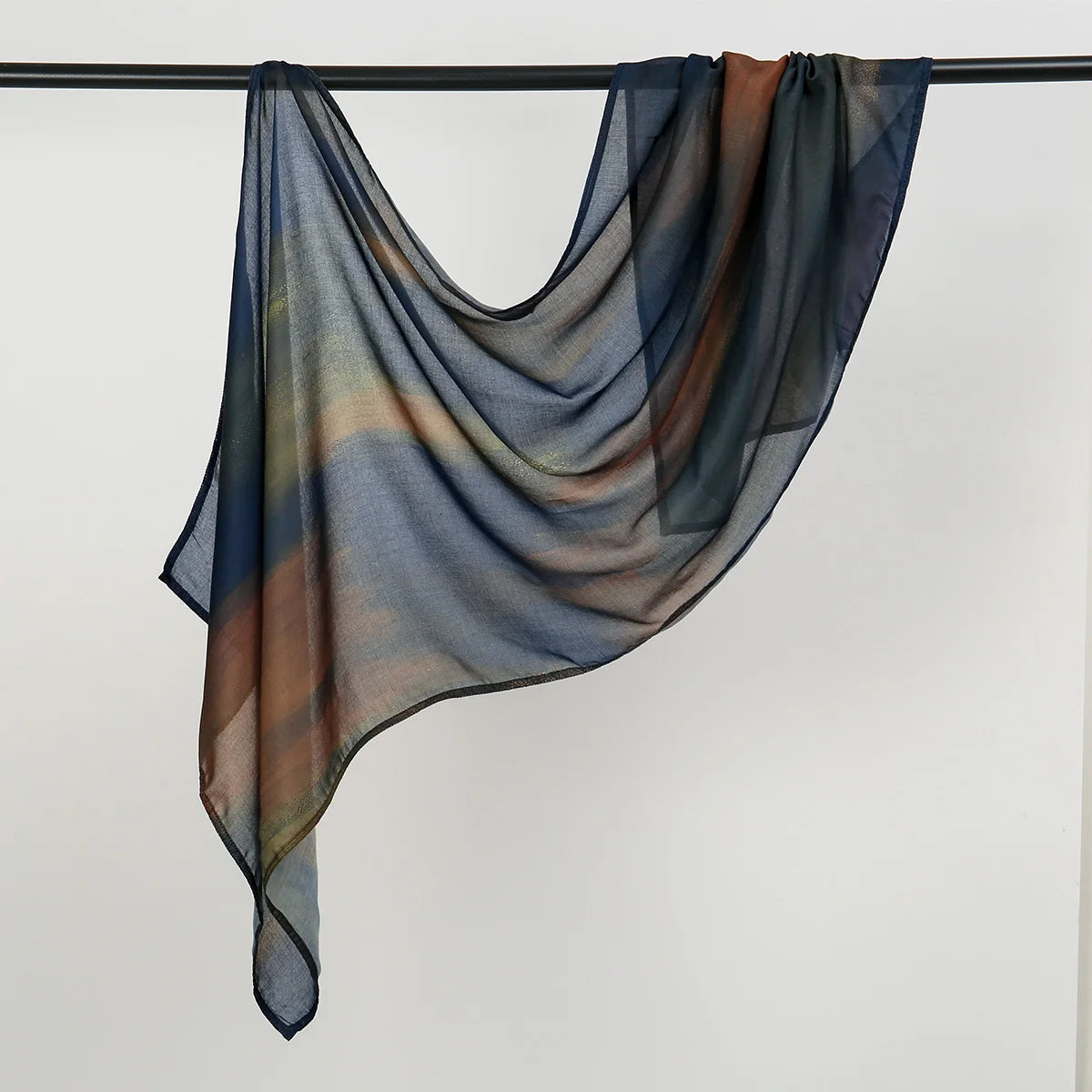 Durchscheinender, fließender Hijab-Schal in blauen, orangefarbenen und grauen Aquarelltönen an einer Wäscheleine.