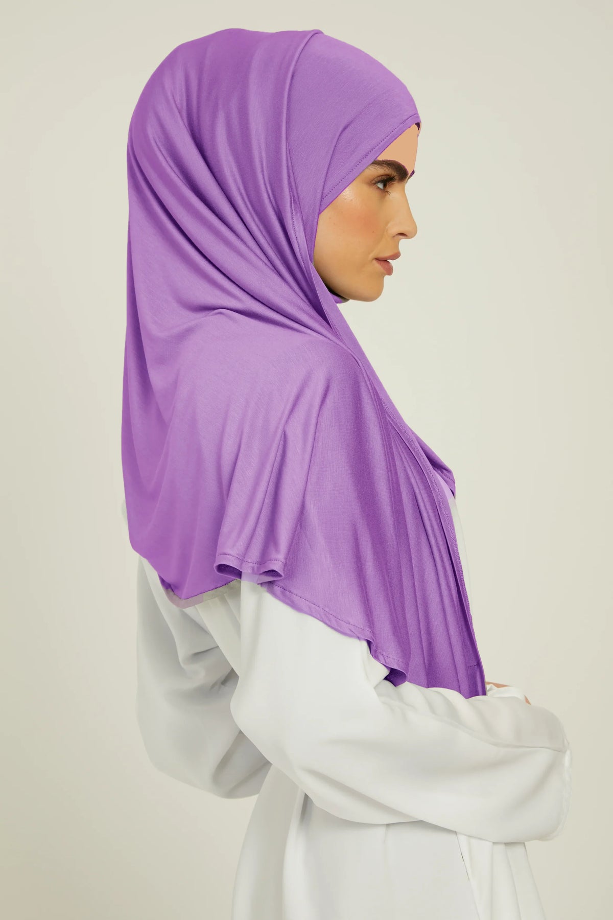 Eine Frau mit lila Hijab-Schal und weißem Oberteil, Profilansicht.