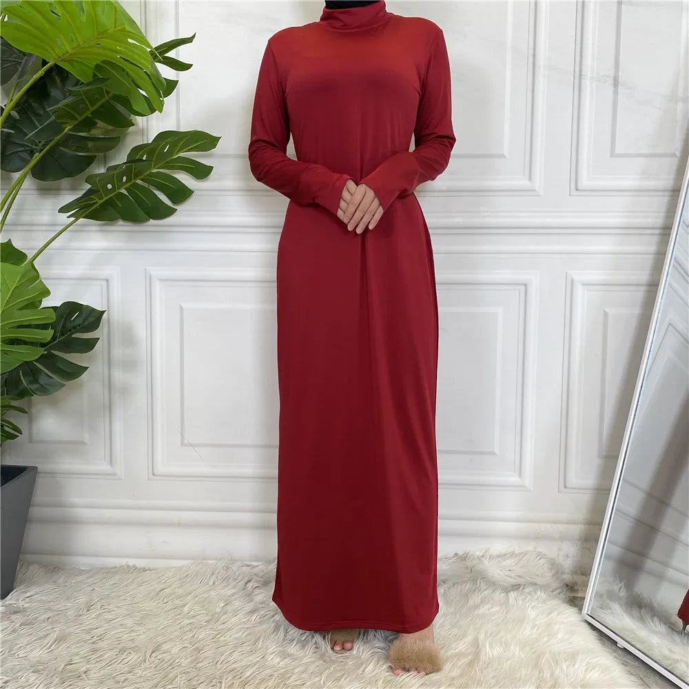 Eine Frau in einem langärmeligen, dunkelroten, langarmigen Abaya-Kleid vor einer weißen Paneelwand.