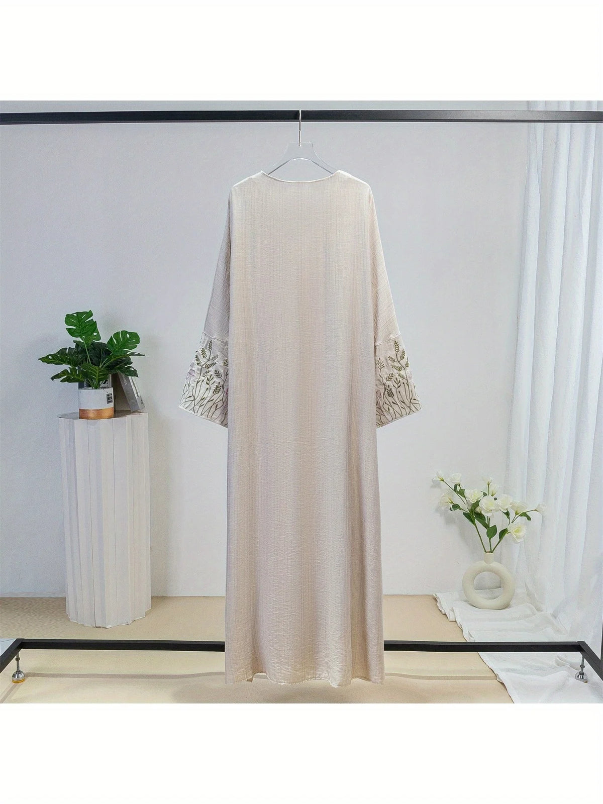 Beige bestickter lockerer Kaftan-Abaya an einem Haken vor weißem Hintergrund
