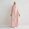 Eine Frau in einem rosa, sch ömmernden Abaya mit gerafften Ärmeln vor einer weißen Wand.