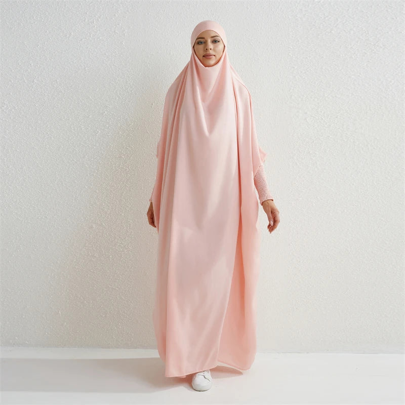 Eine Frau in einem rosa, sch ömmernden Abaya mit gerafften Ärmeln vor einer weißen Wand.
