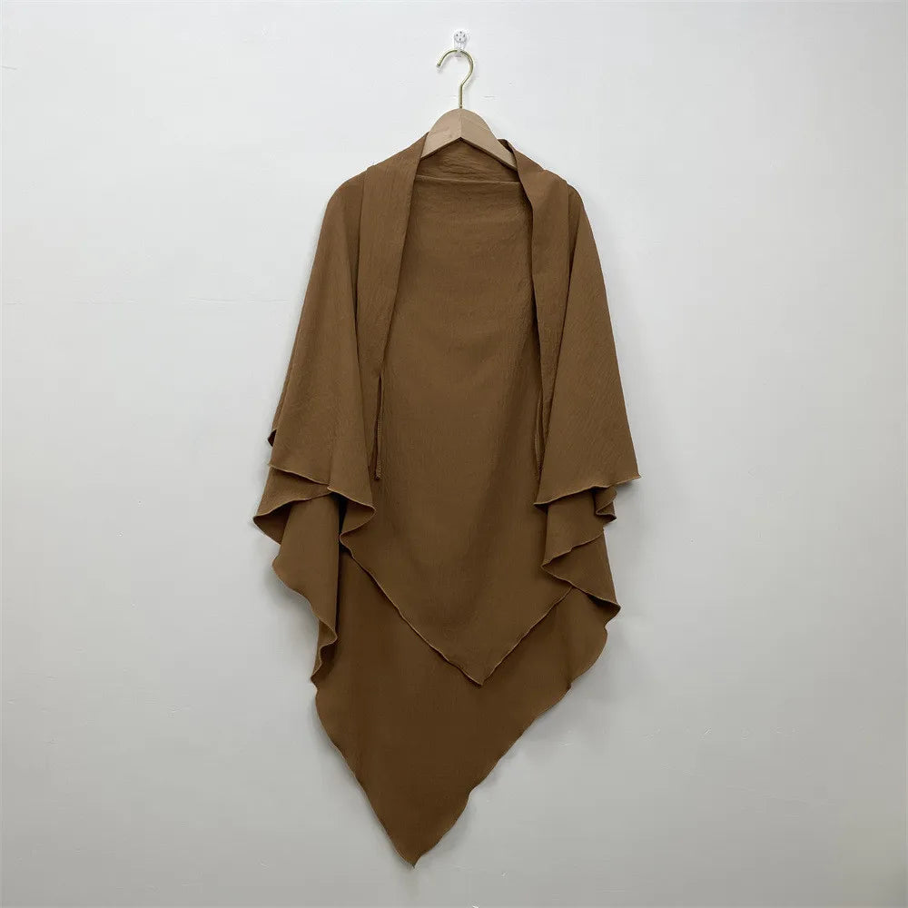 A brown two-layer everyday hijab scarf draped on a hanger against a white wall.