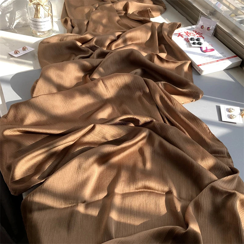 Ein drapiertes Stück braunes, gerafftes Satin-Chiffon-Stoff wird auf einer weißen Oberfläche präsentiert.
