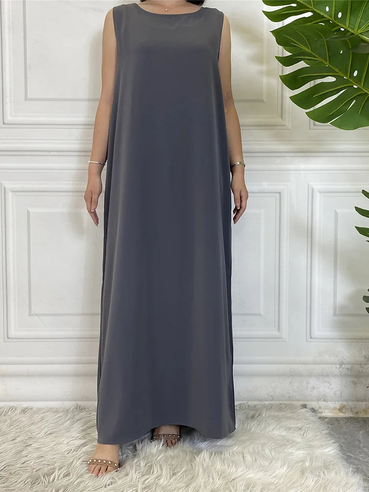 Langes, ärmelloses graues Kaftankleid, präsentiert vor einer weißen Paneelwand.