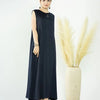 A woman wearing a navy blue flowing modest abaya dress stands next to a tall vase of dried beige ornamental grass.