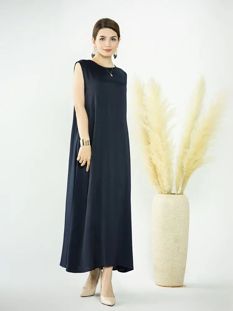 A woman wearing a navy blue flowing modest abaya dress stands next to a tall vase of dried beige ornamental grass.