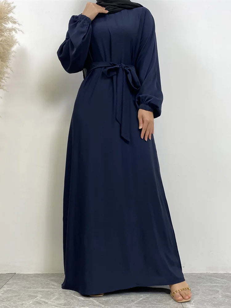 Eine Frau in einem dunkelblauen marokkanischen Kaftan-Abaya mit langen Ärmeln und gebundener Taille vor weißem Hintergrund