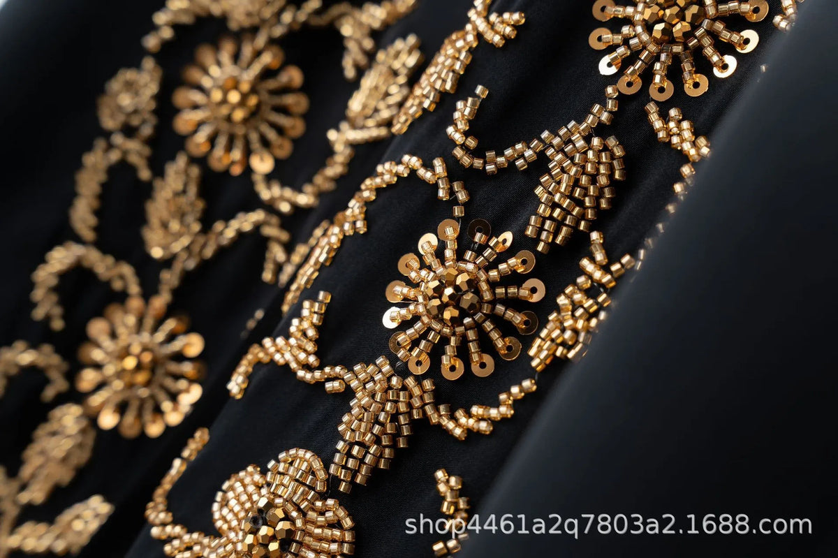 Close-up of gold floral beaded embroidery on a black fabric, likely part of an abaya set.