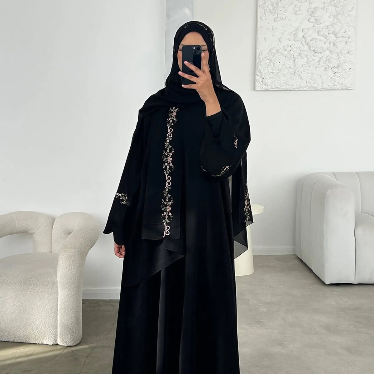 امرأة ترتدي فستان حجاب أسود أنيق مع تطريز زهري واقفة في الداخل.