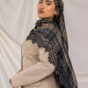 A woman wearing a beige blazer and a plaid hijab scarf with black lace detailing against a white background.
