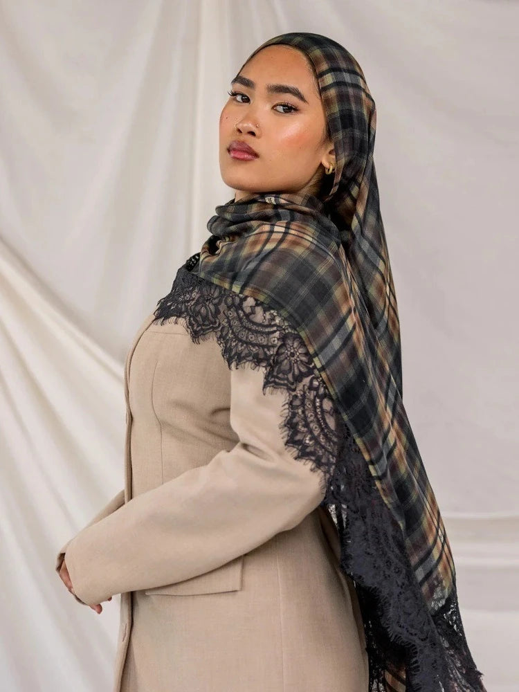 A woman wearing a beige blazer and a plaid hijab scarf with black lace detailing against a white background.