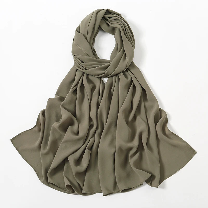 Ein drapiertes olivgrünes Chiffon-Schal oder Hijabgewebe, gefaltet und vor weißem Hintergrund präsentiert.