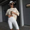 Una mujer viste una camiseta básica de algodón beige oversize y leggings blancos en un pasillo moderno.