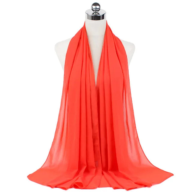 A bright coral red chiffon hijab scarf draped around a mannequin's neck.