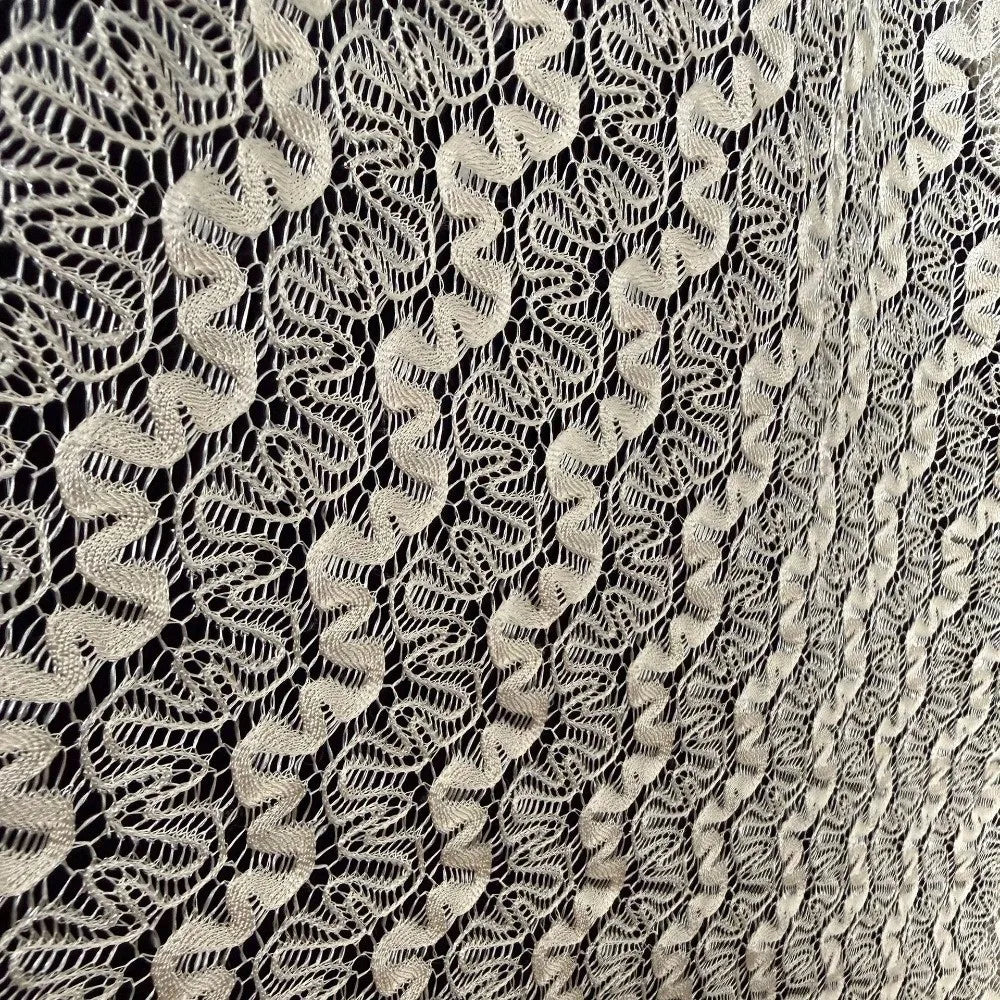 Primer plano de tejido de encaje de color crema y elegante con intrincados patrones geométricos.